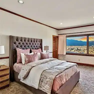 Bed with pink comforter in bedroom with large window